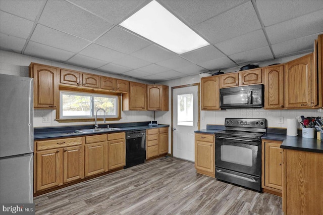 kitchen with a drop ceiling, black appliances, sink, and wood-type flooring