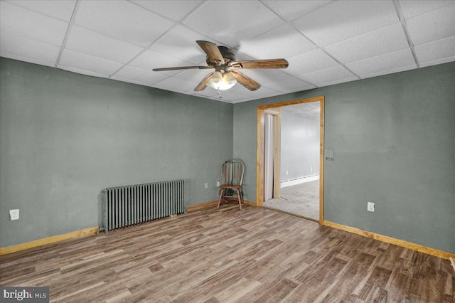 spare room with hardwood / wood-style floors, a drop ceiling, radiator heating unit, and ceiling fan