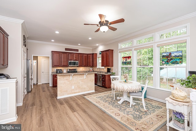 kitchen featuring crown molding, stainless steel appliances, a kitchen island, a breakfast bar, and light hardwood / wood-style flooring