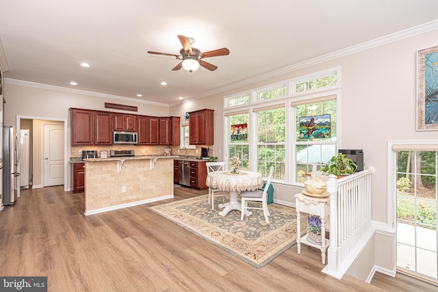 kitchen featuring stainless steel appliances, a breakfast bar, ornamental molding, light hardwood / wood-style flooring, and a center island