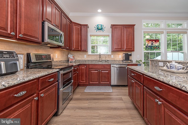 kitchen with stainless steel appliances, light hardwood / wood-style floors, light stone counters, sink, and crown molding