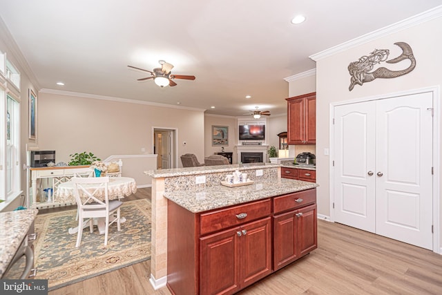 kitchen featuring a center island, light stone counters, ornamental molding, ceiling fan, and light hardwood / wood-style flooring