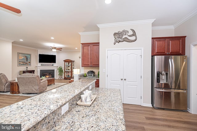 kitchen featuring light stone countertops, crown molding, stainless steel fridge, and light hardwood / wood-style flooring