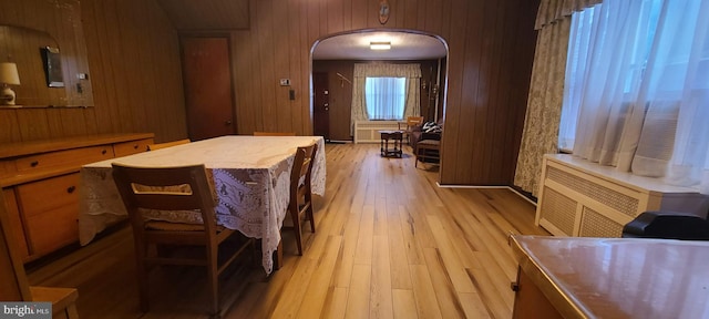 dining room featuring wood walls, radiator heating unit, and light wood-type flooring