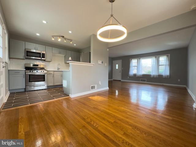 kitchen featuring gray cabinetry, dark hardwood / wood-style floors, backsplash, and stainless steel appliances