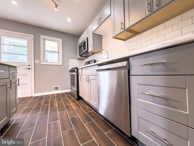 kitchen featuring appliances with stainless steel finishes, dark hardwood / wood-style flooring, gray cabinetry, and backsplash