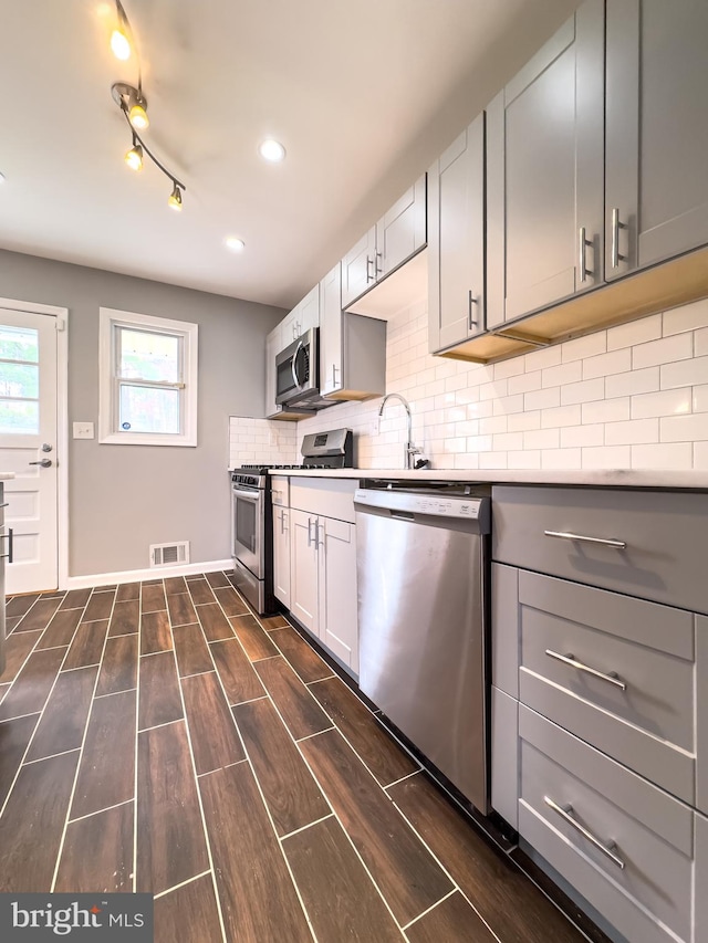 kitchen featuring sink, dark hardwood / wood-style floors, gray cabinets, tasteful backsplash, and stainless steel appliances