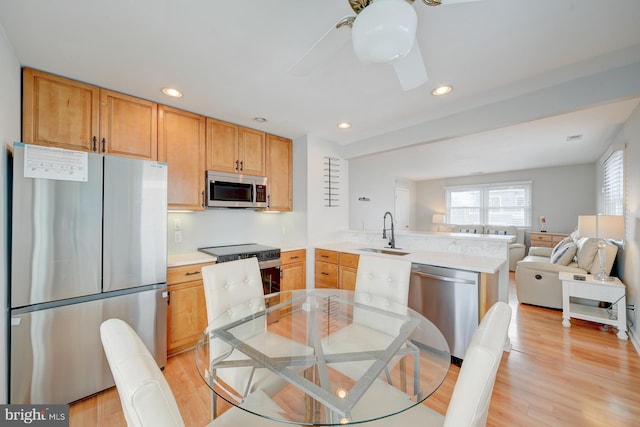 kitchen with sink, light brown cabinets, stainless steel appliances, kitchen peninsula, and light hardwood / wood-style floors