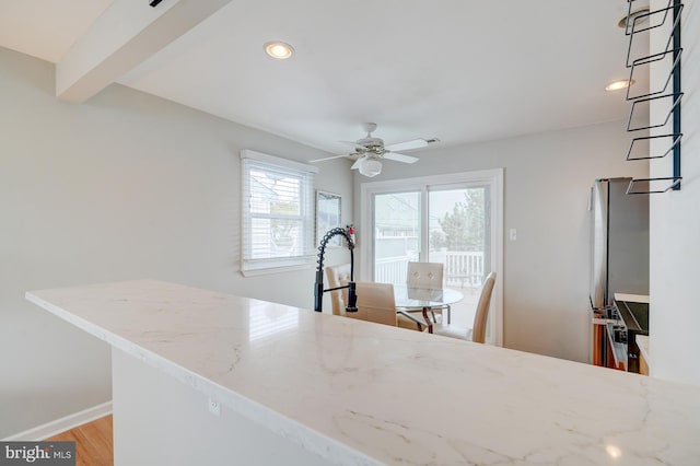 kitchen featuring beam ceiling, light wood-type flooring, light stone counters, and ceiling fan