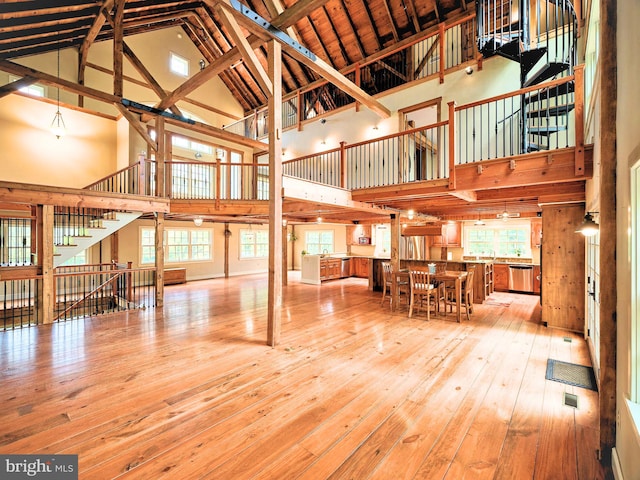 interior space with high vaulted ceiling, plenty of natural light, beamed ceiling, and light hardwood / wood-style floors