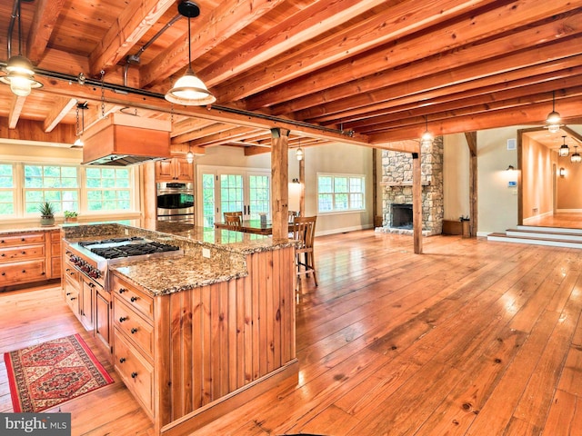 kitchen with stainless steel appliances, dark stone counters, custom range hood, beam ceiling, and decorative light fixtures