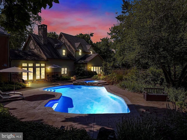 pool at dusk with a patio and an in ground hot tub