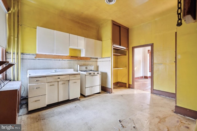 kitchen with white stove, white cabinetry, tile walls, and sink