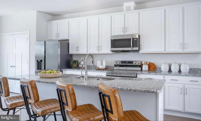 kitchen featuring a kitchen island with sink, a kitchen bar, stainless steel appliances, and white cabinetry