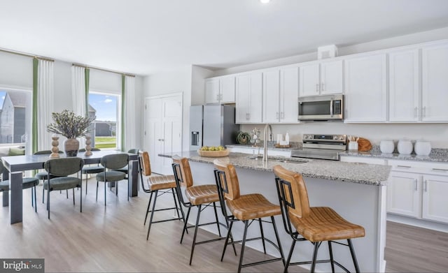 kitchen featuring white cabinets, stainless steel appliances, light wood-type flooring, and an island with sink