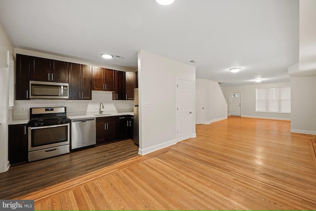 kitchen featuring light wood-type flooring, tasteful backsplash, dark brown cabinets, stainless steel appliances, and sink