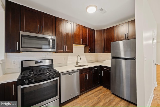 kitchen with sink, light hardwood / wood-style flooring, decorative backsplash, appliances with stainless steel finishes, and dark brown cabinets