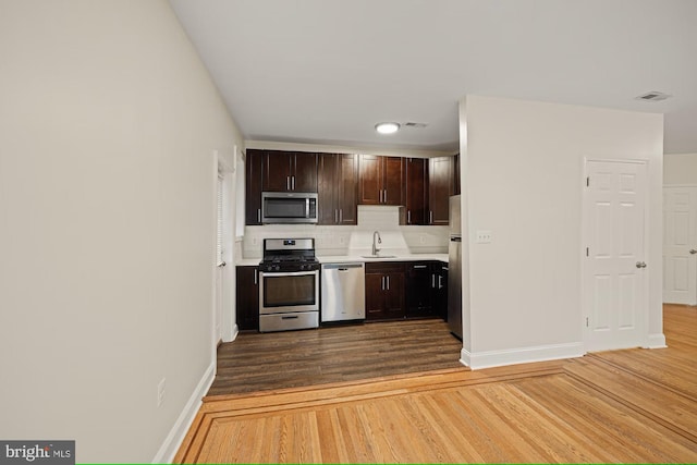 kitchen with sink, hardwood / wood-style flooring, decorative backsplash, appliances with stainless steel finishes, and dark brown cabinetry