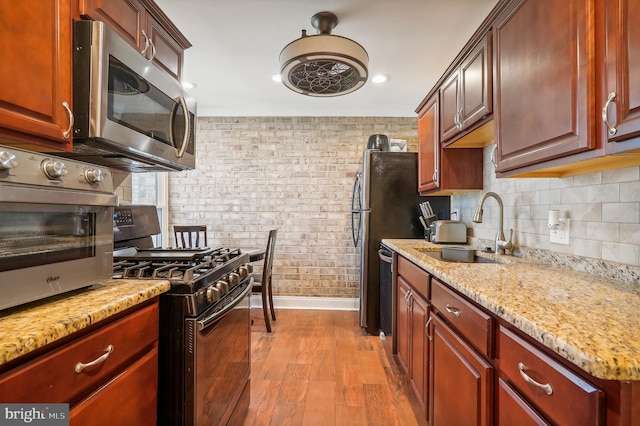 kitchen with black gas range, light stone countertops, light wood-type flooring, sink, and brick wall