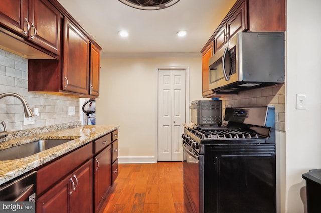 kitchen with ornamental molding, sink, light stone countertops, appliances with stainless steel finishes, and light hardwood / wood-style floors