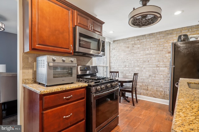 kitchen with light hardwood / wood-style flooring, light stone countertops, stainless steel appliances, and tasteful backsplash