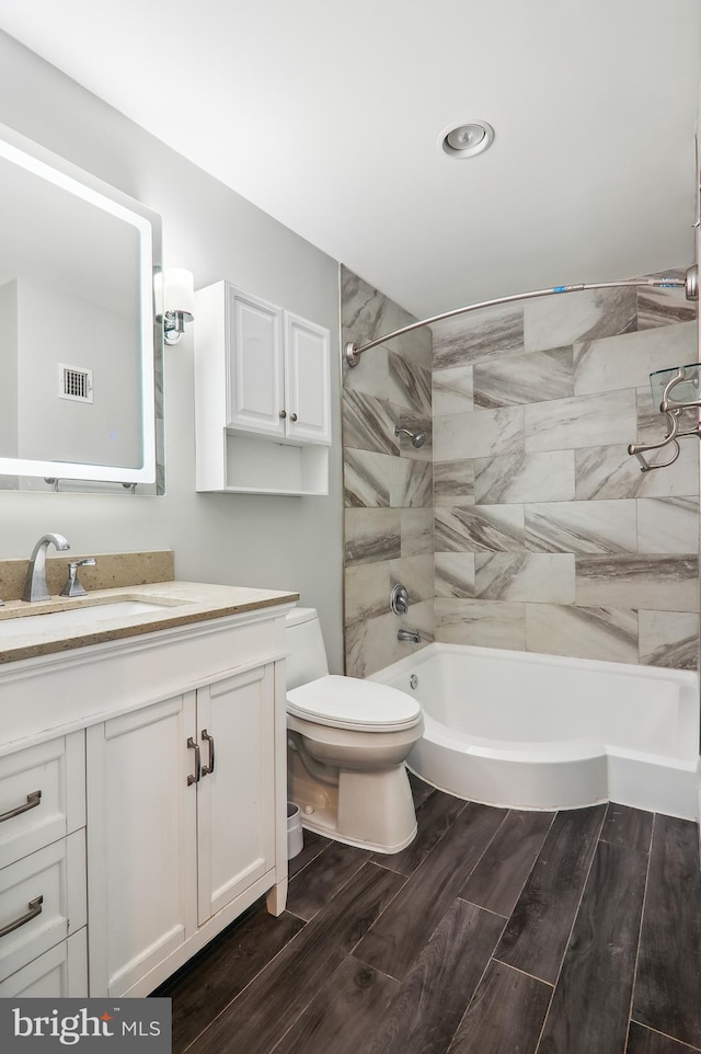 full bathroom with toilet, tiled shower / bath, hardwood / wood-style floors, and vanity