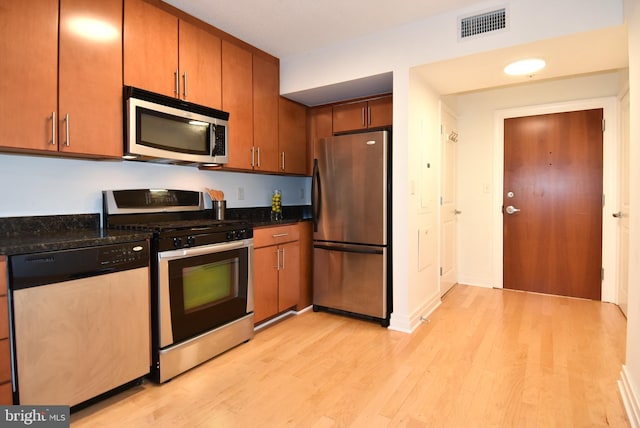 kitchen with dark stone countertops, light hardwood / wood-style floors, and appliances with stainless steel finishes