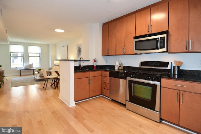 kitchen featuring light hardwood / wood-style flooring, dark stone countertops, stainless steel appliances, and sink