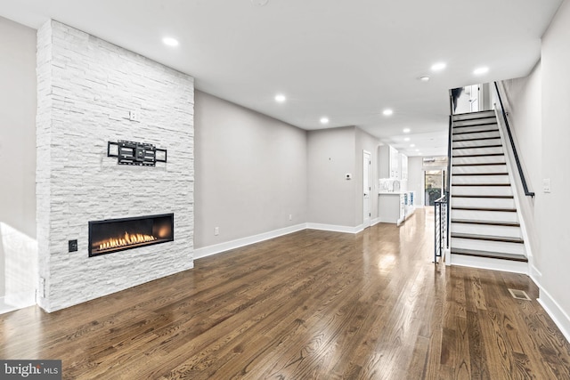 unfurnished living room with a stone fireplace and dark hardwood / wood-style floors