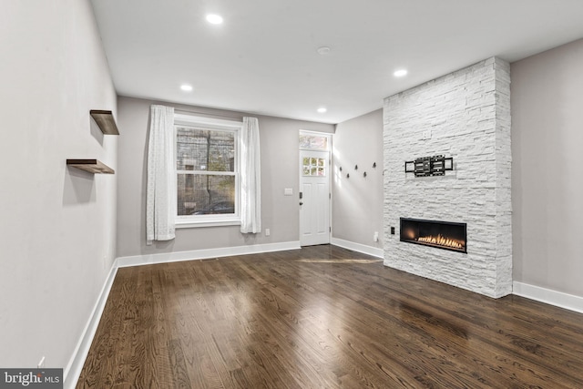 unfurnished living room with a stone fireplace and dark hardwood / wood-style floors