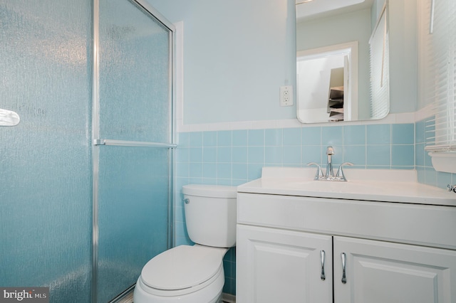 bathroom featuring vanity, toilet, a shower with shower door, and tile walls