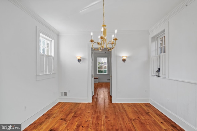 unfurnished dining area featuring hardwood / wood-style floors, crown molding, and a chandelier