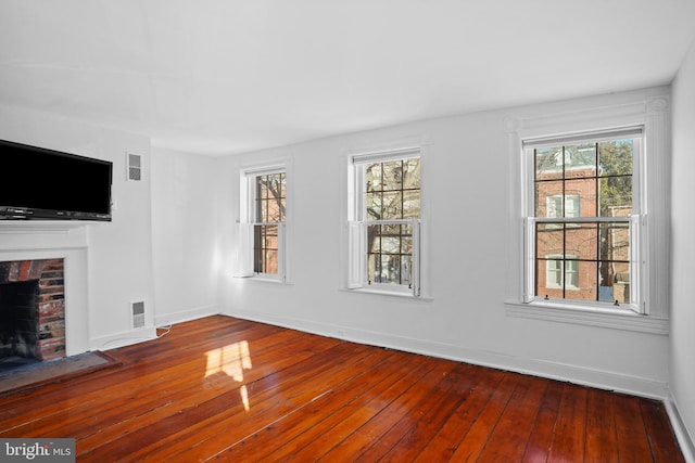 unfurnished living room featuring a healthy amount of sunlight, hardwood / wood-style floors, and a brick fireplace