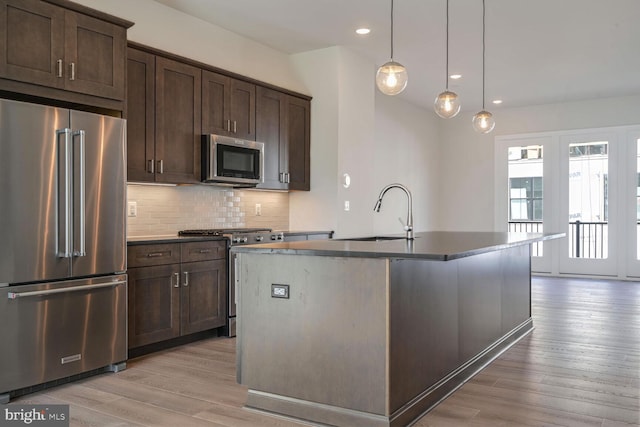 kitchen featuring a center island with sink, light wood-type flooring, pendant lighting, sink, and high end appliances