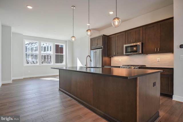 kitchen with dark wood-type flooring, stainless steel appliances, and a center island with sink