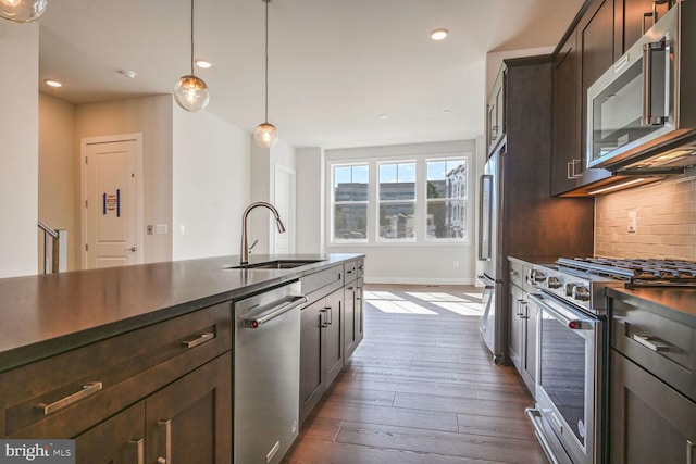 kitchen with tasteful backsplash, hanging light fixtures, dark hardwood / wood-style floors, sink, and premium appliances