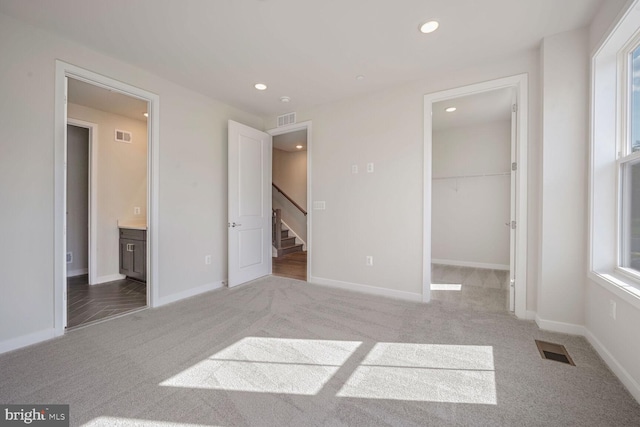 unfurnished bedroom featuring light carpet, a walk in closet, multiple windows, and ensuite bath