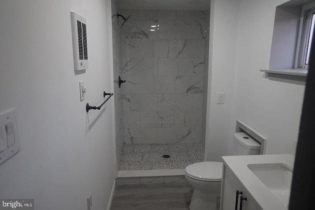 bathroom with hardwood / wood-style floors, vanity, toilet, and tiled shower