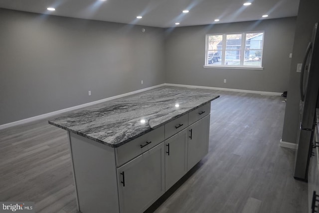 kitchen with white cabinets, stone countertops, a center island, and wood-type flooring