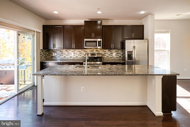 kitchen featuring dark hardwood / wood-style flooring, plenty of natural light, a center island with sink, and appliances with stainless steel finishes