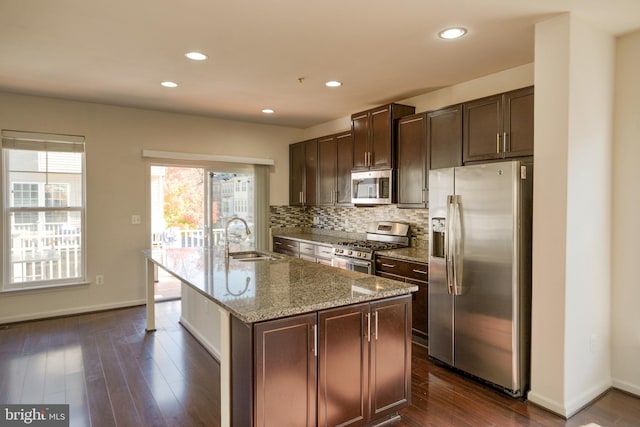 kitchen with appliances with stainless steel finishes, dark brown cabinetry, dark hardwood / wood-style flooring, sink, and a kitchen island with sink