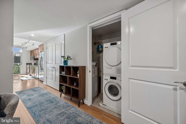 laundry room with water heater, stacked washing maching and dryer, and light wood-type flooring