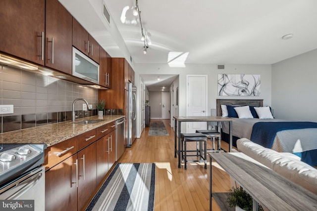 kitchen with decorative backsplash, appliances with stainless steel finishes, light stone counters, sink, and light hardwood / wood-style flooring