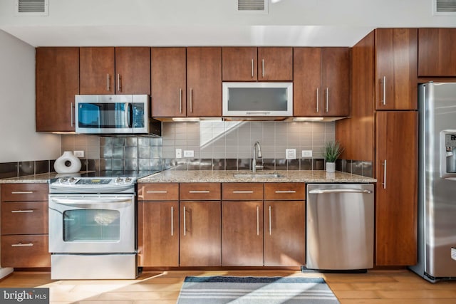 kitchen featuring light hardwood / wood-style flooring, sink, appliances with stainless steel finishes, stone countertops, and backsplash