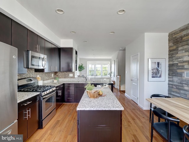 kitchen featuring decorative backsplash, dark brown cabinetry, stainless steel appliances, and light wood-type flooring