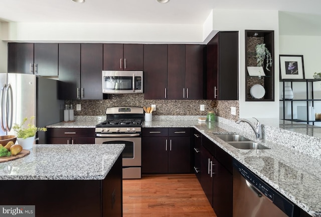 kitchen featuring dark brown cabinets, sink, appliances with stainless steel finishes, light stone counters, and light hardwood / wood-style floors