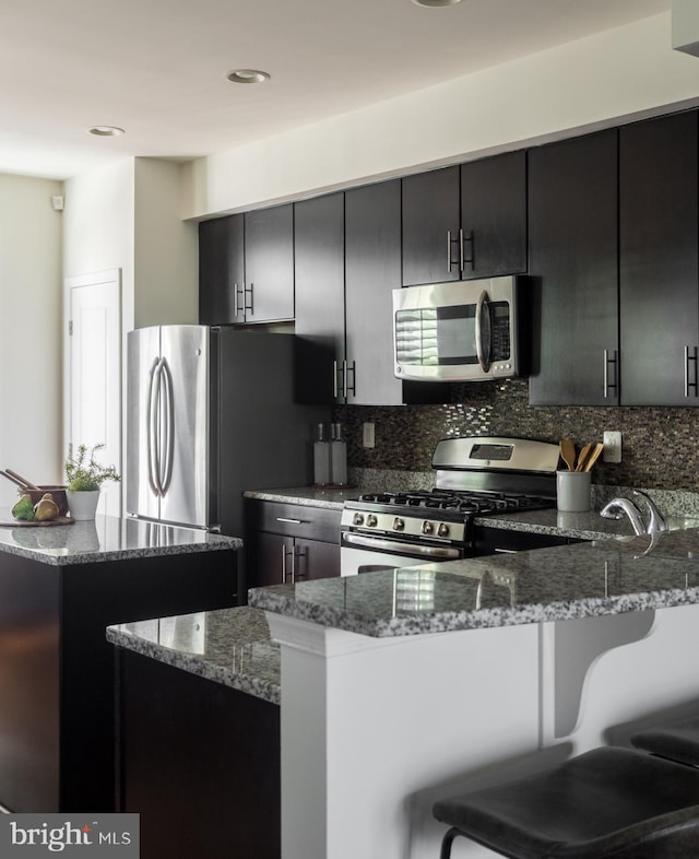 kitchen featuring kitchen peninsula, tasteful backsplash, appliances with stainless steel finishes, light stone countertops, and a kitchen bar