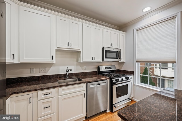 kitchen with sink, dark stone countertops, appliances with stainless steel finishes, white cabinets, and ornamental molding