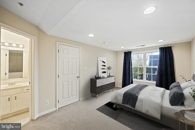 bedroom with connected bathroom, light colored carpet, and sink