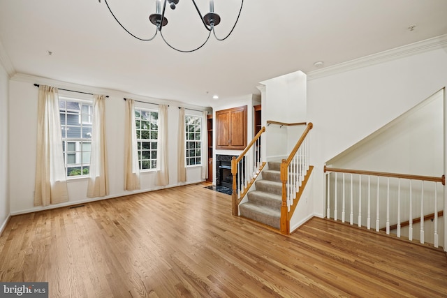 unfurnished living room featuring light wood-type flooring, crown molding, and a notable chandelier